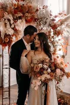 a bride and groom standing next to each other in front of a floral arch with flowers