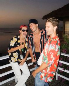 three men standing next to each other on a balcony near the ocean at night time