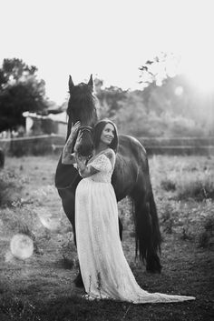 black and white photograph of a woman in a dress standing next to a horse with her hands on her face