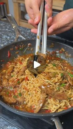 someone is stirring noodles with tongs in a wok