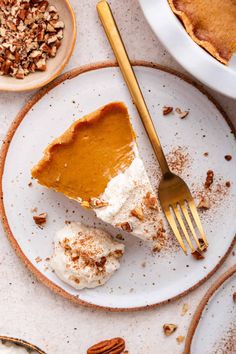 a slice of pumpkin pie on a plate with a fork next to it and pecans in the background