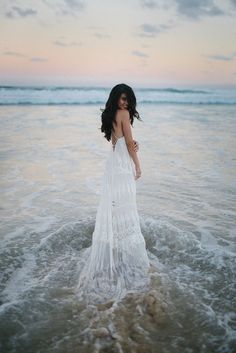 a woman standing in the ocean wearing a white dress