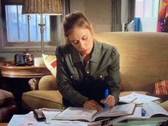 a woman sitting at a table in front of an open book and writing on it