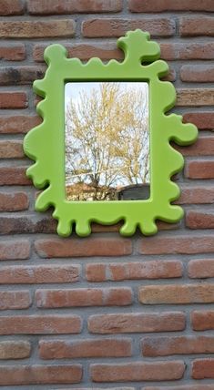 a green mirror mounted to the side of a brick wall with a tree in the reflection