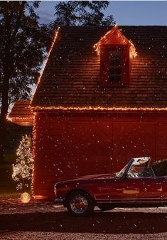 a red car parked in front of a barn with christmas lights