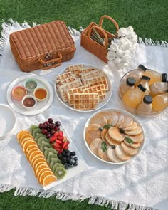 a table topped with lots of food on top of a white blanket next to a picnic basket