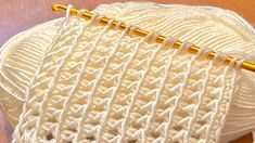 a close up of a knitting needle on top of a white knitted object with gold pins