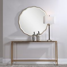 a mirror sitting on top of a wooden table next to a white lamp and two vases