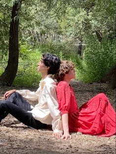 two people sitting on the ground in front of trees