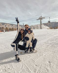 a woman and two children on a snowboard at the top of a ski slope