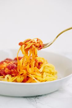 a white bowl filled with pasta and sauce on top of a marble countertop next to a gold fork