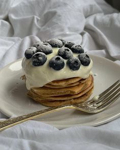 a white plate topped with pancakes covered in frosting and blueberries next to a fork