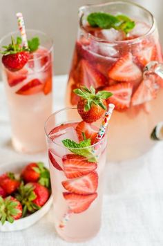 two glasses filled with water and strawberries on top of a white table cloth next to plates