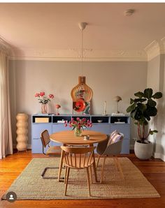 a dining room table and chairs in front of a large window with potted plants