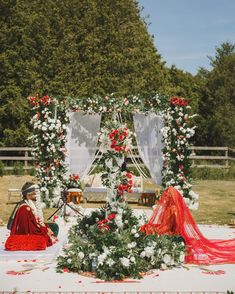 a man and woman sitting on the ground in front of a flower covered structure with flowers