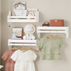 three baby clothes are hanging on the wall next to a teddy bear and bookshelf