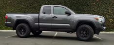 a gray truck parked in a parking lot next to a hedge covered wall and shrubbery