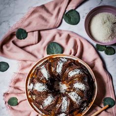 a bundt cake with powdered sugar on top sits in a bowl next to a pink towel