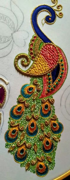 the embroidery design is being worked on by someone using scissors and thread to make it look like a peacock