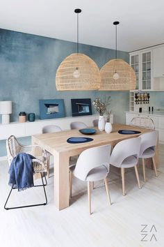 a dining room table and chairs in front of a blue wall with wicker hanging lights