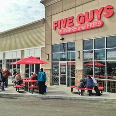 people are sitting at red picnic tables outside the five guys