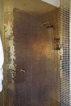 a bathroom with gold tiled walls and a shower head in the corner, next to a white towel