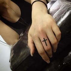 a woman's hand with a cross tattoo on her left thumb and black leather purse