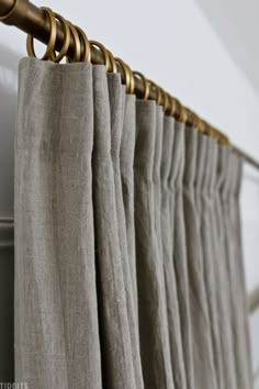 curtains hanging on a rod in front of a white wall with gold hardware and curtain rods