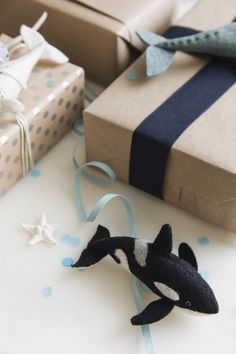 an orca stuffed animal sitting next to presents on a white table with blue ribbon