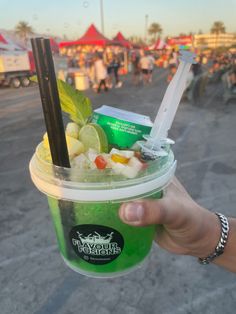 a person holding up a green drink with strawberries and limes in it at an outdoor event