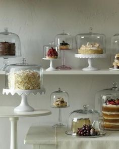 several cakes and desserts under glass domes on shelves in a white walled kitchen area