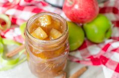 an apple cider with apples in the background and cinnamon sticks next to it on a checkered table cloth