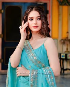 a woman in a blue sari holding her hand up to her face and looking at the camera