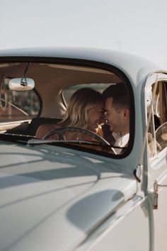 a man and woman are sitting in the back seat of a vintage car looking at each other