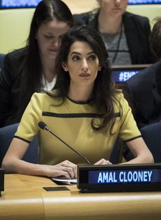 a woman sitting at a table in front of a microphone with the name amal clooney on it