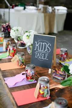 a wooden table topped with jars filled with candy and candies next to a sign that says kids table