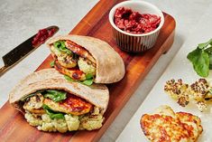 two burritos on a cutting board with a bowl of salsa