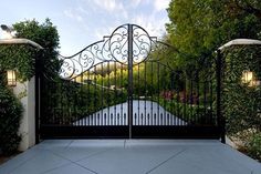 an iron gate in front of a house with trees and bushes on either side of it