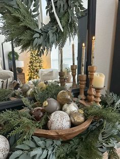 a wooden bowl filled with christmas ornaments and greenery on top of a table next to a mirror