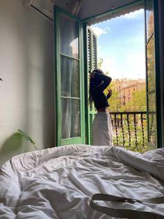 a woman standing on top of a bed in front of a window with green shutters