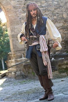 a man dressed as captain jack sparrow in front of an old stone building with chains