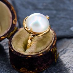 a ring with a white pearl sits in an open box on top of a rock