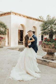 a bride and groom standing in front of a building with potted plants on the side