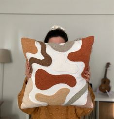 a woman holding up a pillow with an abstract design on it