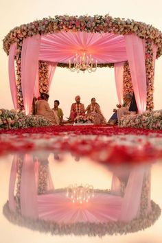 a group of people sitting on top of a red carpet under a pink and white canopy