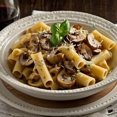 a white bowl filled with pasta and mushrooms on top of a wooden table next to a glass of wine