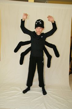 a young boy standing in front of a white backdrop wearing a black hat and spider costume