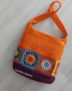 an orange handbag with multicolored flowers on the front and sides, hanging from a string