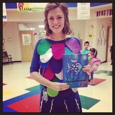 a woman holding a book in her hands while standing on the floor with other children