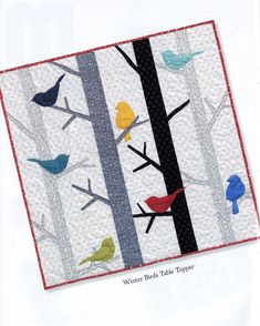 a quilted wall hanging with birds perched on the branches and in the background is a forest